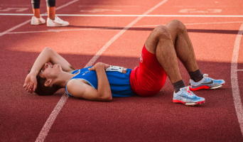 an athlete laying down on a track appearing exhausting after running a race