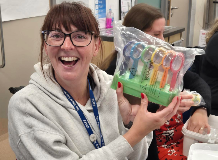 a happy teacher holds up a pack of colourful magnifying glasses in a classroom setting