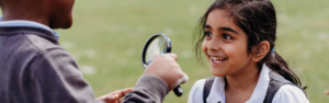 Children using magnifying glasses outdoors during a primary science activity, observing and discussing findings together