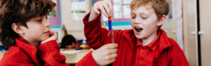 Two primary school children investigating magnetism using magnets and paperclips in a classroom.
