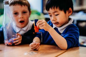 Two children observing a bar magnet and attaching paperclips